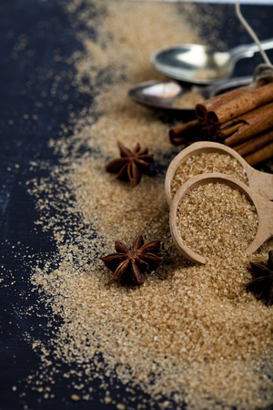 Brown cane sugar, cinnamon sticks and star anise closeup on black board background. With copy space.の写真素材