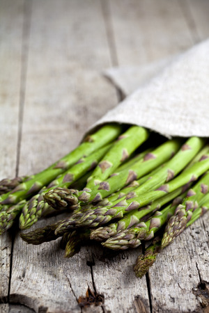 Bunch of fresh raw garden asparagus closeup and linen napkin on rustic wooden table background. Green spring vegetables. Edible sprouts of asparagus. With copy space.の写真素材