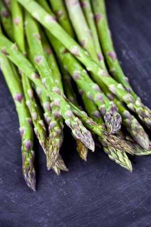 Organic fresh raw garden asparagus closeup on black board background. Green spring vegetables. Edible sprouts of asparagus. With copy space.の写真素材
