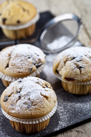 Two fresh homemade muffins with sugar powder and metal strainer closeup on black board background.の写真素材
