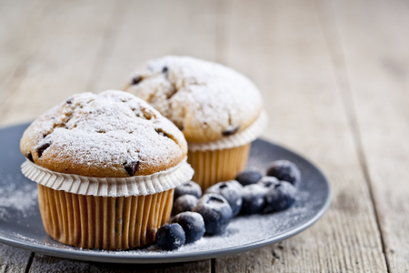 Homemade fresh muffins with sugar powder and blueberries on ceramic plate closeup on rustic wooden table background.の写真素材