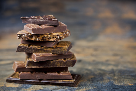 Broken chocolate stacked on black background. Chocolate bar pieces heap witn cinnamon powder. Sweet...