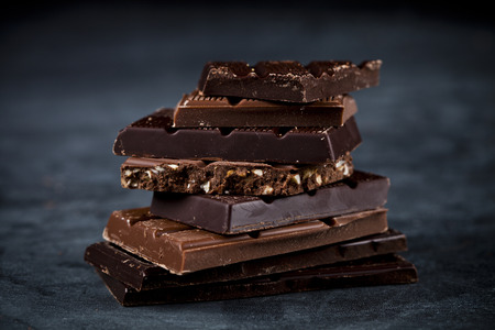Chunks of broken chocolate stacked on black board. Chocolate bars pieces stack on black background. Sweet food photo concept.の写真素材
