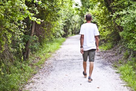 Man walking on path in summer green park. Peaceful atmosphere. Rest from loud city. Spending time alone in beautiful, sunny spring day. With copy space.の写真素材
