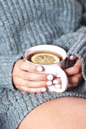 Female hands holding mug of hot tea with lemon in morning. Young woman relaxing tea cup on hand. Good morning tea or have a happy day message concept.の写真素材