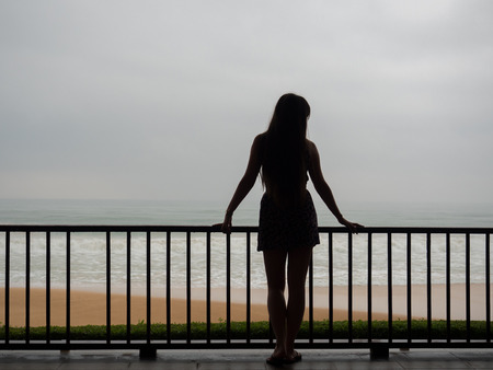 Beautiful young girl or woman standing on a balcony or terrace overlooking the seaの写真素材