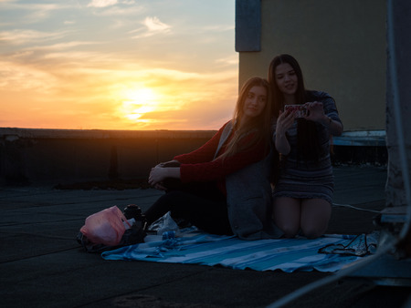 Girlfriends on the roof are photographed against the sunset. The roof of a house.の写真素材