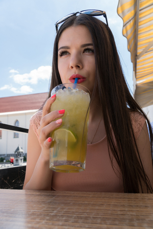 A girl is drinking a tropical mojito in a summer cafe. A girl with glasses, a pink dress and bright red lips.の写真素材