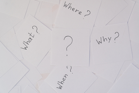 White square sheets of paper with questions spread out in chaotic order on a yellow background. Main questions.の写真素材