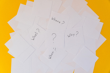 White square sheets of paper with questions spread out in chaotic order on a yellow background. Main questionsの写真素材