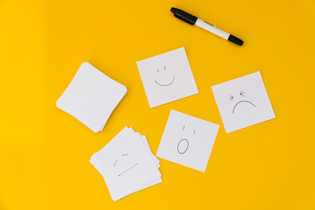 Emotions drawn on white sheets of paper are laid out on a yellow backgroundの写真素材
