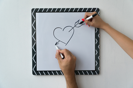 A guy and a girl draw a heart with markers on a white board. A mask and a female hand against a white board with a symbol of love.の写真素材