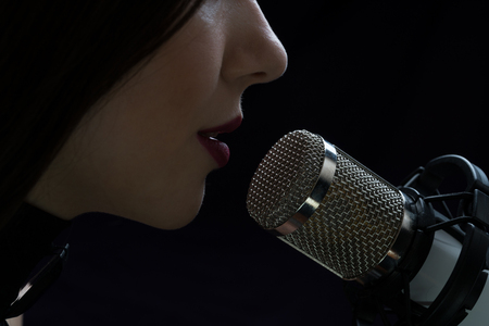 Singer in front of a microphone. Isolated on a dark background.の写真素材