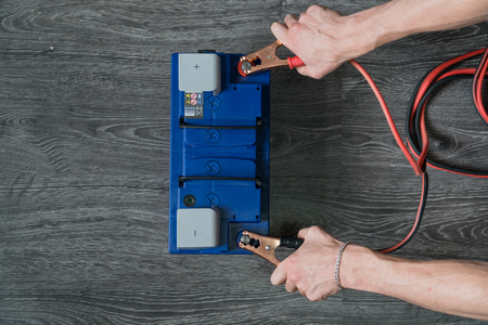 The male hand connects the terminals to the cars batteries on a wooden background