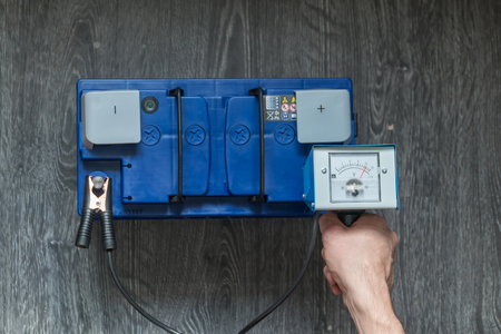 A mans hand holds a car battery tester on a wooden backgroundの写真素材