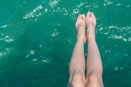 young female legs hanging over the sea water.の写真素材