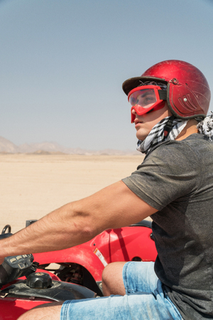Young guy during desert excursion by quad - Man in helmet and adventure clothes in exotic scenarios - Concept of activity holiday, freedom and adventure.の写真素材
