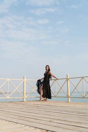 A girl in a swimsuit and a cloak is standing on the pier and meets the dawn.の写真素材