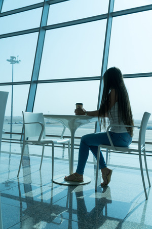 Girl is holding a glass of coffee in airport's business lounge with aircraft.の写真素材