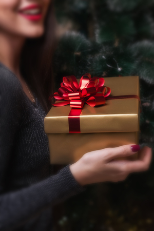 A girl is holding a gift, sitting under a Christmas tree.