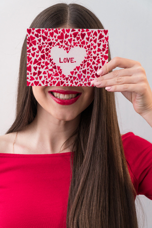 Portrait of a sweet perfect girl smiling at camera with heart shaped paper in her hands. Valentines Day or Womens Day conceptの写真素材