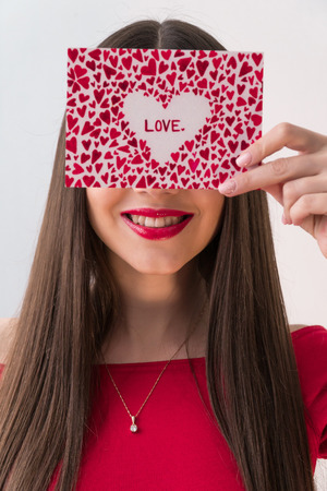Portrait of a sweet perfect girl smiling at camera with heart shaped paper in her hands. Valentines Day or Womens Day conceptの写真素材