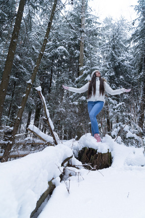 Beautiful girl with long dark hair in a white jacket walking in a winter forest during a snowfallの写真素材