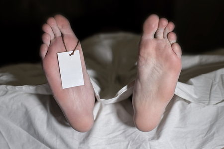 Dead man lying on the floor under white cloth with blank tag on feet - retro style. The concept of...