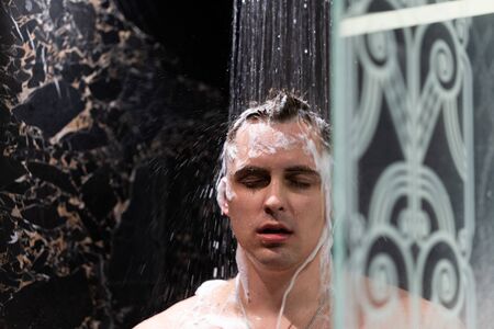 The guy washes in the shower. Shower with dark wallsの写真素材