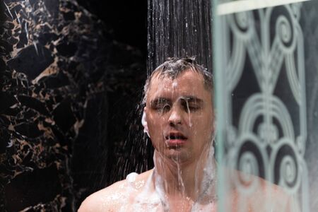 The guy washes in the shower. Shower with dark wallsの写真素材
