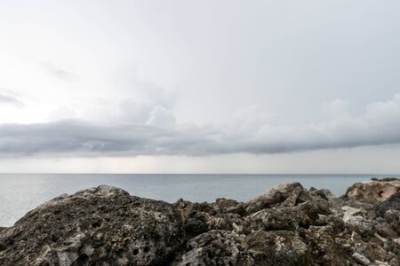 In the foreground in focus is a rocky shore. In the distance, the ocean and clouds.の写真素材