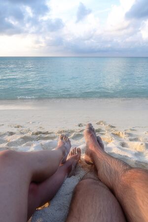 The legs of a young couple in love, who sit on the beach and see off the sunset.