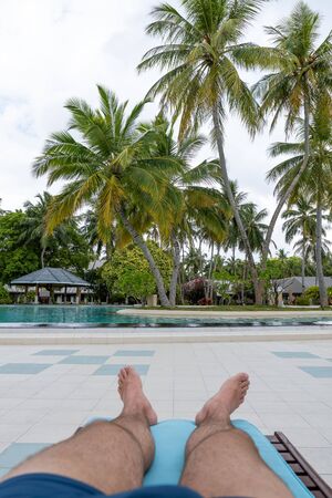 Pool with a first-person view. One can see the male legs on a deck chairの写真素材