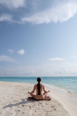 Meditation - Yoga woman meditating at serene beach. Girl relaxing in lotus pose in calm zen moment in the ocean water during yoga holidays resort retreat.の写真素材