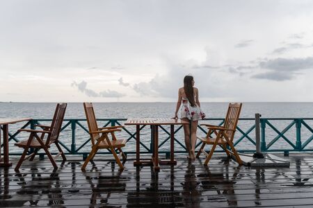 A young girl in a dress is standing in a sea restaurant. The island has rainy weatherの写真素材
