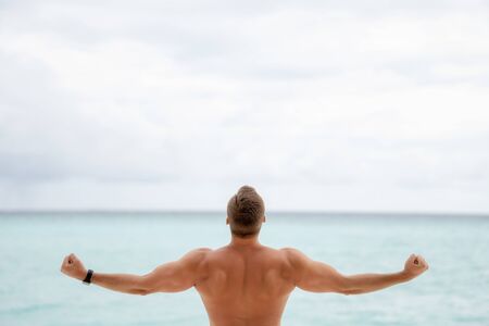 Inflated back and arms of a young guy on the background of the ocean and overcast skyの写真素材