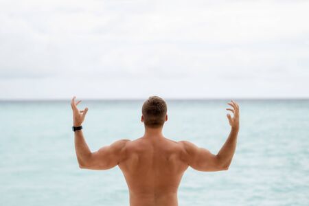 Inflated back and arms of a young guy on the background of the ocean and overcast skyの写真素材