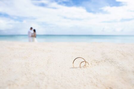 Wedding rings on the white sand. In the background the newlyweds and the ocean.の写真素材