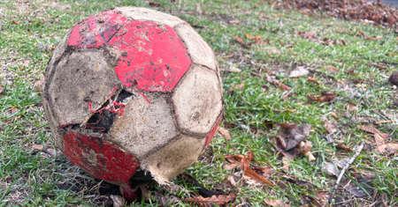 Old torn shabby soccer ball on ground. Grey and red.の写真素材