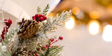 Christmas tree branch decoration with pine cone, red berries, artificial snow and blurred background with golden bokehの写真素材