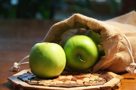 Organic green apples in a burlap sack on a wooden table close up.の写真素材
