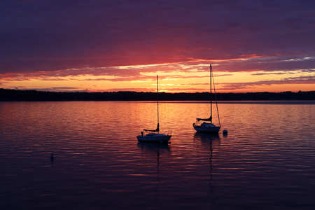 Amazing summer evening landscape with group of drifting yachts on a lake during spectacular sunset. Bright sky reflects in the lake water.の写真素材