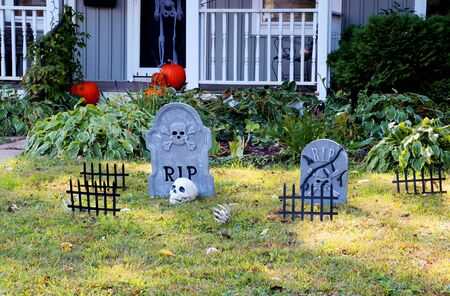 Front yard of private house decorated by fake skull, bones hands, tombstones and grates, pumpkins on the porch for a old american trick-or-treat Halloween tradition.の写真素材