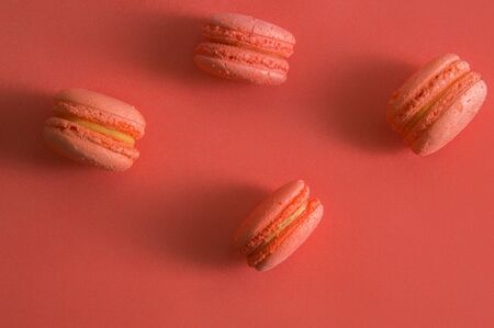 Flat lay. Close up, macro. Sweet french macarons color living coral. Cookies laid out on the edge. Background color living coral 2019.の写真素材