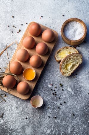 Flat lay. Traditional breakfast, still life. A dozen farm eggs in a wooden tray, baguette with cheese and spices. Copy space.の写真素材