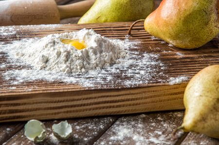 Close up, macro. Broken quail egg in a hill of white flour, surrounded by ripe large pears. Rustic still life. Brown wooden background.の写真素材