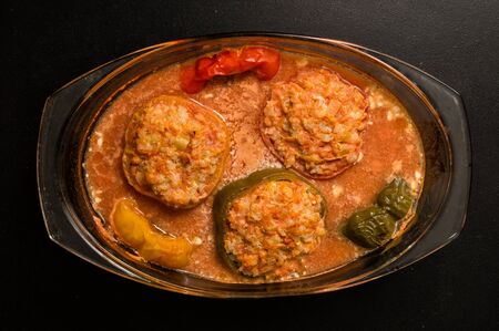 Flat lay, top view. Close up, still life. Cooking a Bulgarian Traditional Dinner. Stuffed bell peppers baked in tomato sauce in a transparent saucepan. Black background.の写真素材