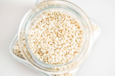 Top view, flat lay. Close up, macro. Glass jar filled with sesame seeds. White background.の写真素材