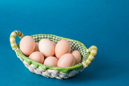 Macro, close up. Farm brown eggs in a wicker basket lined with checkered fabric. Blue background....