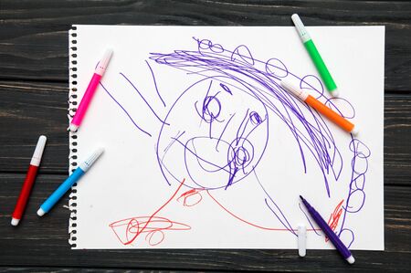 Close up, macro, flat lay. Figure drawn by a 3 year old child. Black table with a white sheet of paper. On it is drawnの写真素材